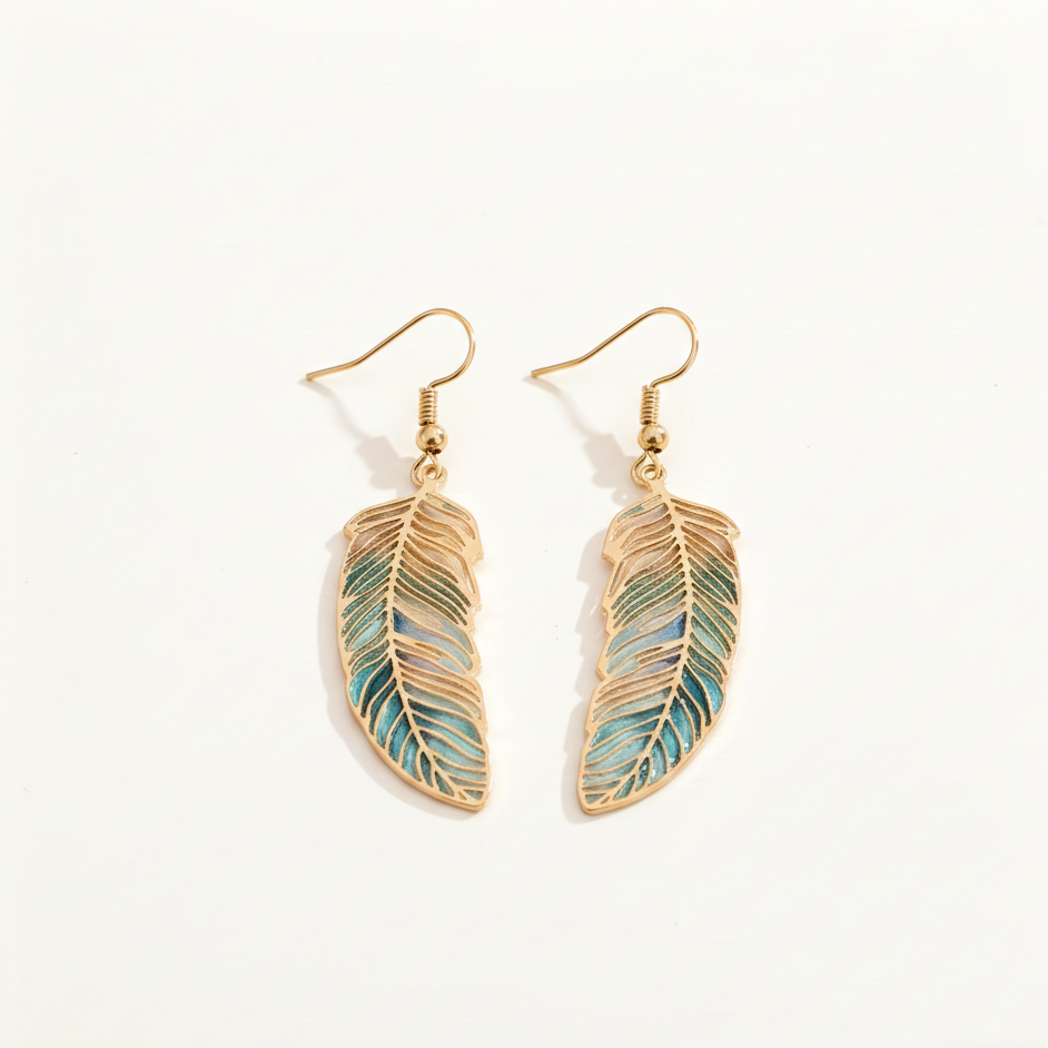 Vue de dessus d'une paire de boucles d'oreilles en forme de plumes posées à plat sur un fond blanc. Les plumes présentent un dégradé de couleurs allant du beige au bleu turquoise avec des nervures dorées.