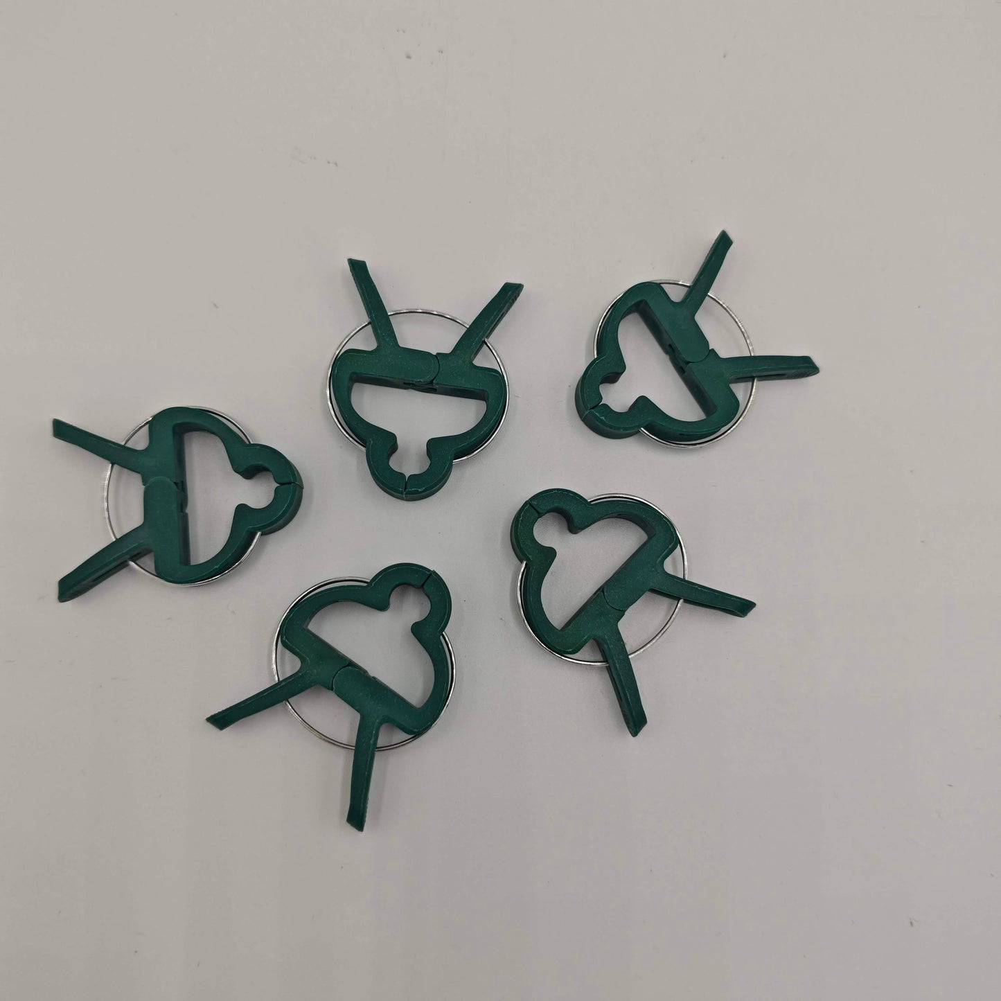 Un lot de cinq clips de support pour plantes en plastique vert avec un ressort métallique, conçus pour fixer les tiges aux tuteurs.