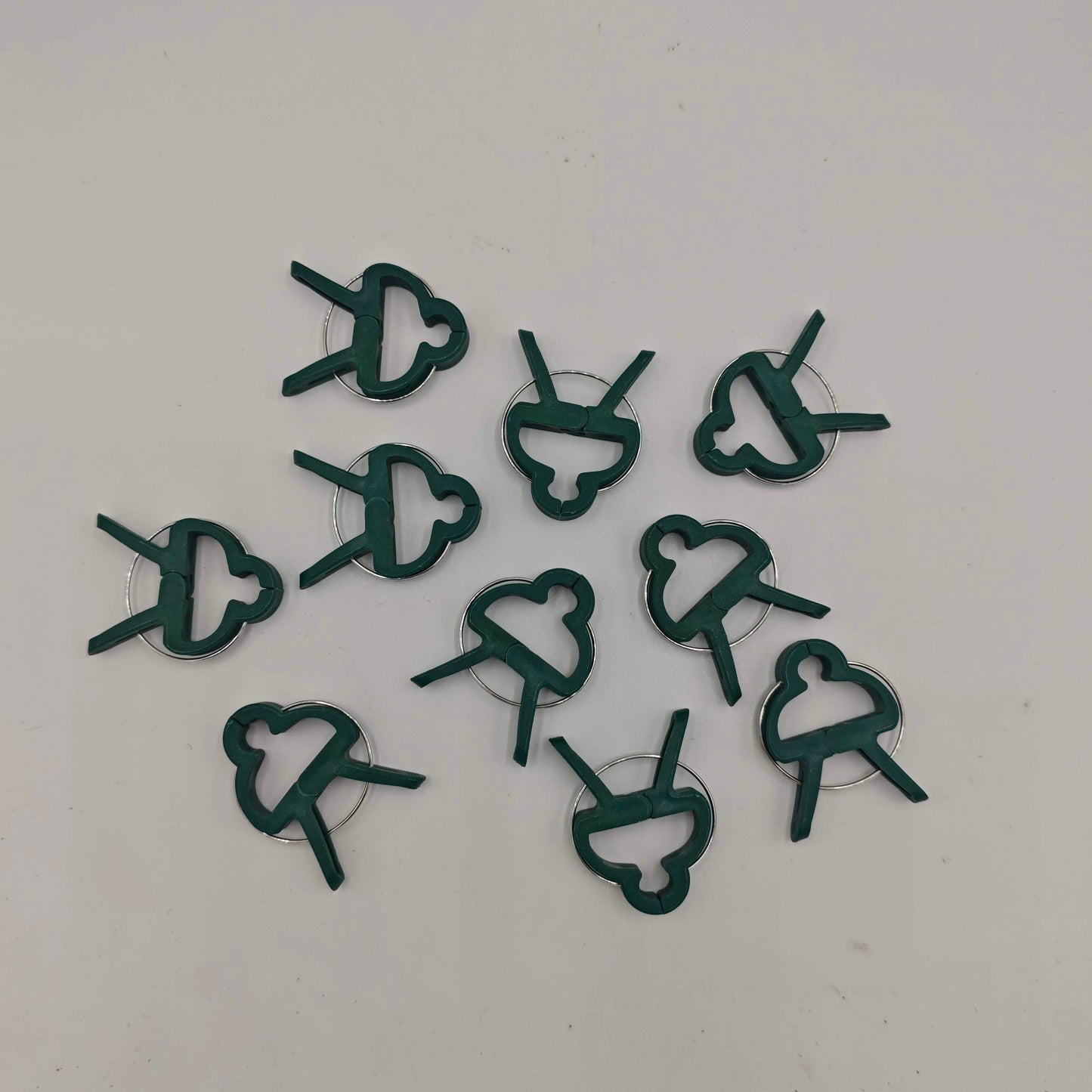 Un lot de dix clips de support pour plantes en plastique vert, avec un design en forme de papillon et un ressort métallique.