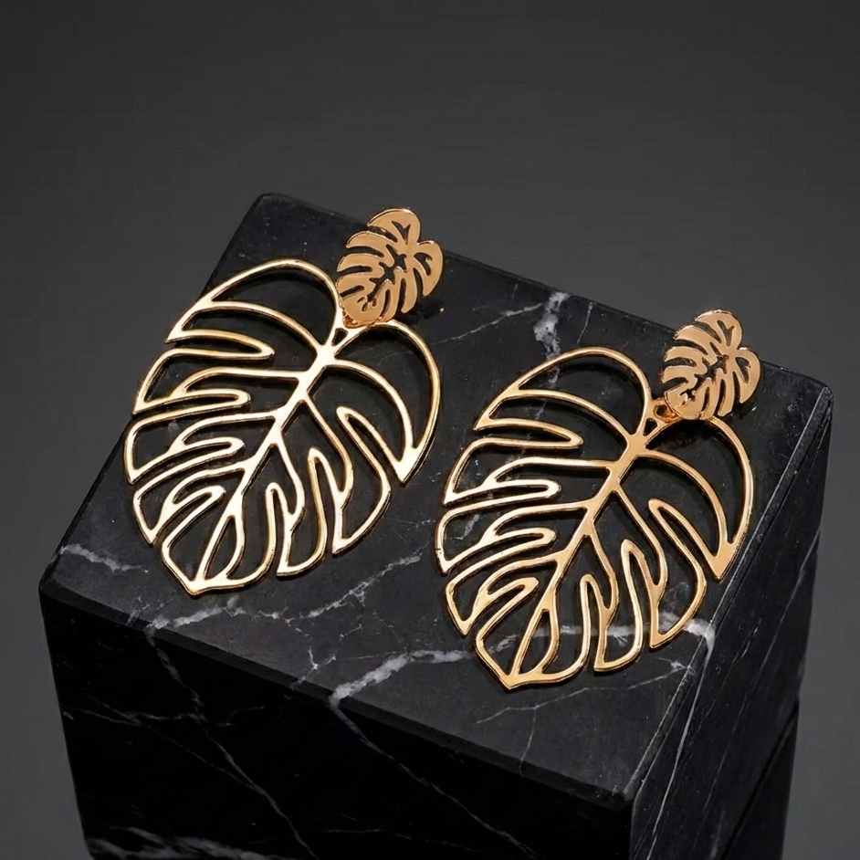 Gros plan sur des boucles d'oreilles motif feuille de Monstera en métal doré, posées sur un cube de marbre noir veiné, offrant un contraste élégant et sophistiqué.