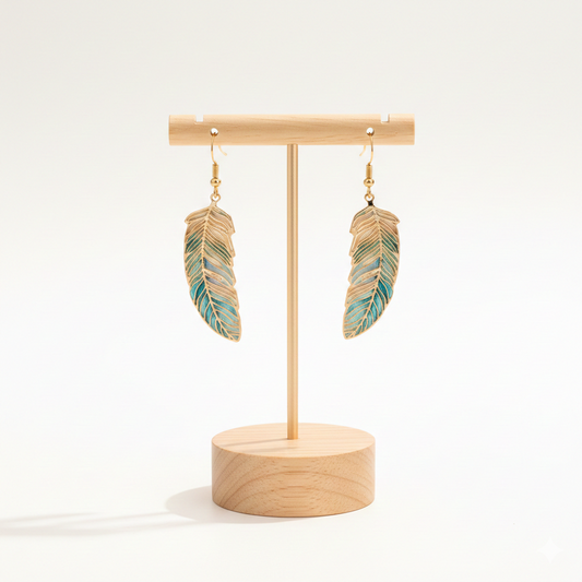Paire de boucles d'oreilles pendantes plumes suspendues à un présentoir à bijoux minimaliste en bois clair sur fond blanc.
