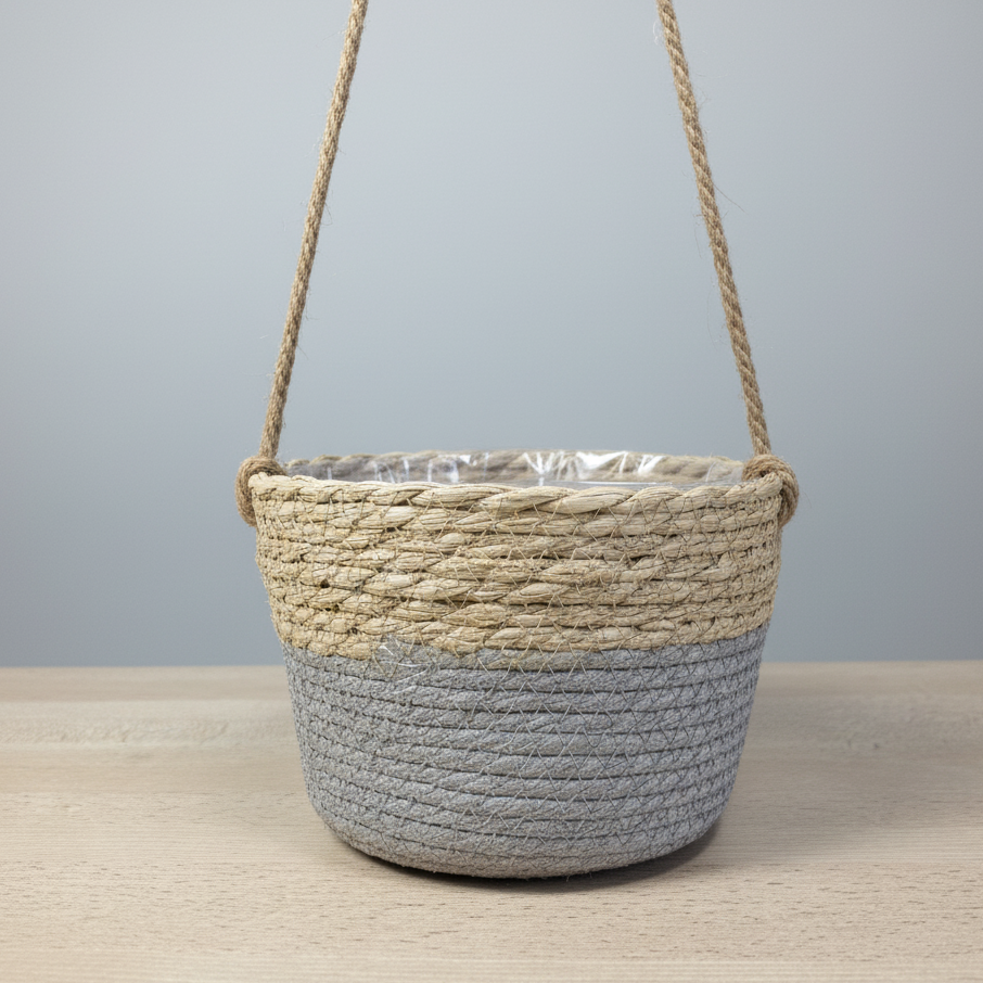 Panier tressé bicolore suspendu (moitié supérieure beige naturel et moitié inférieure gris clair), avec une doublure en plastique transparent visible, posé sur une table en bois clair.