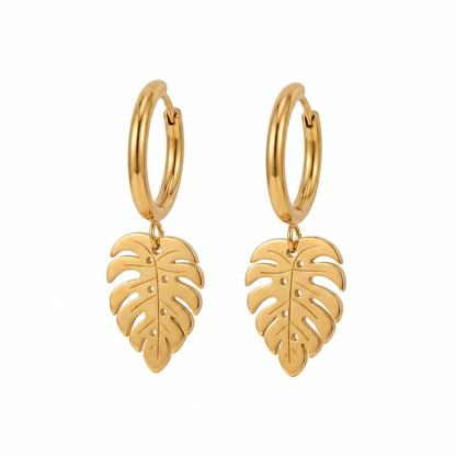 Paire de boucles d'oreilles créoles dorées avec un pendentif en forme de feuille de monstera. Vue de face sur fond blanc uni, fermoir charnière visible.
