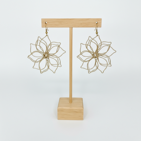 Paire de boucles d'oreilles artisanales en forme de fleur présentées sur un support en bois clair, fond blanc épuré.