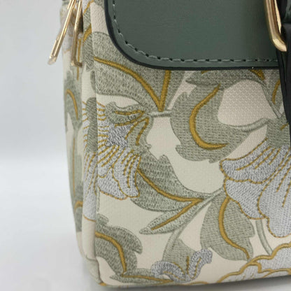 Gros plan sur la broderie d'un sac à main. Le sac est blanc cassé avec un motif de feuilles vertes et jaunes brodées.
