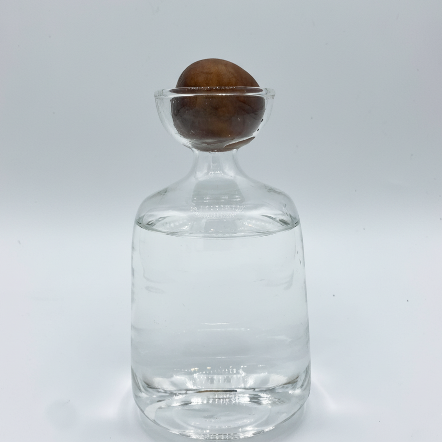 Gros plan sur un noyau d'avocat posé sur le goulot d'un verre en forme de carafe, avec de l'eau au fond, sur un fond blanc.