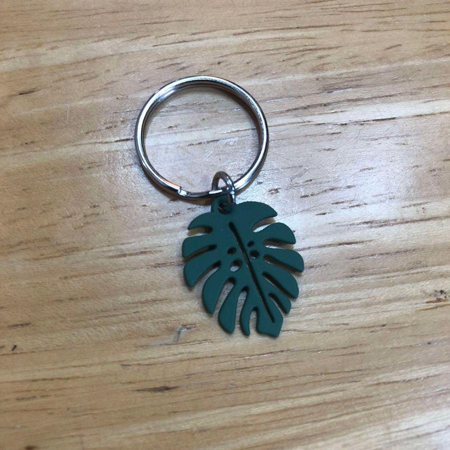 pendentif en forme de feuille monstera vert foncé posé sur une table en bois