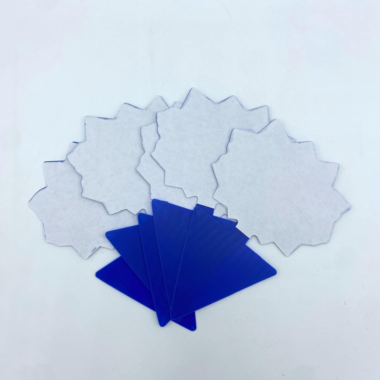 Un éventail de pièges à insectes blancs en forme d'étoile et une pile de pièges bleus, présentés sur un fond blanc et uni.