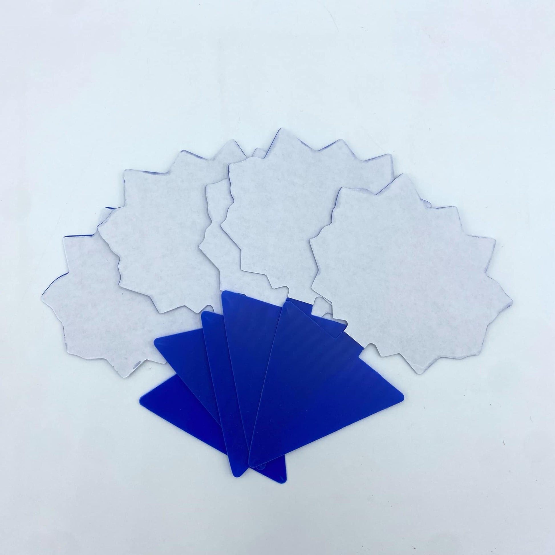 Un éventail de pièges à insectes blancs en forme d'étoile et une pile de pièges bleus, présentés sur un fond blanc et uni.